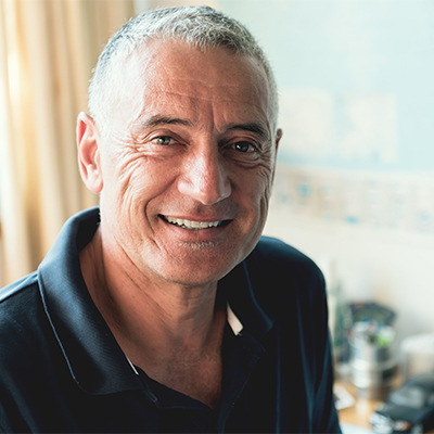 Middle-aged man with short gray hair smiling indoors, wearing a dark polo shirt with soft natural lighting in the background.