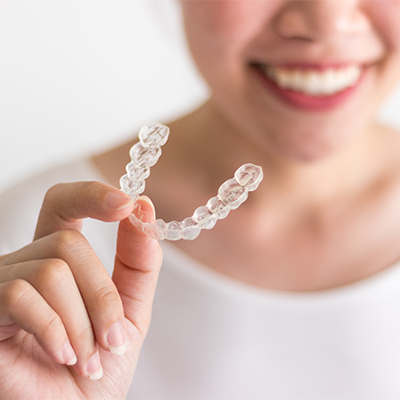 Woman smiling and holding a clear aligner tray, highlighting orthodontic treatment with invisible braces.