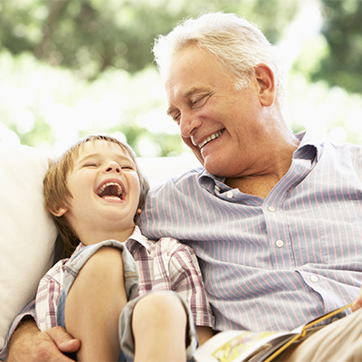 Grandfather and young grandson sitting on a couch, laughing and sharing a joyful moment together in a bright indoor space.